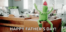 kermit the frog is sitting on a desk in a living room and waving .