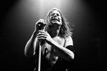 a man with long hair singing into a microphone in a black and white photo