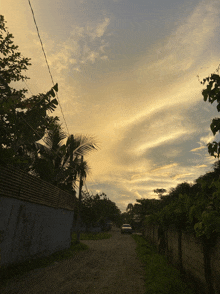 a car is driving down a dirt road with a sunset sky in the background
