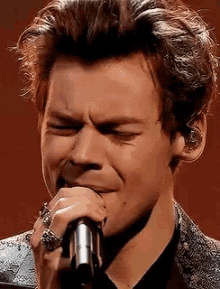harry styles is crying while singing into a microphone on stage .