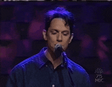 a man singing into a microphone with 75 nbc written on the bottom
