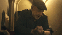 a man wearing a flat cap is looking down at his watch