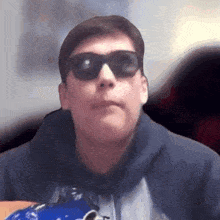 a man wearing sunglasses and a hoodie is holding a blue bag .