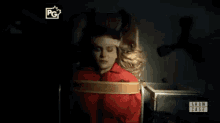 a woman is tied up in a chair with a show case logo on the bottom right