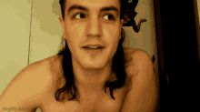 a shirtless man with long hair is smiling in front of a frog on a wall