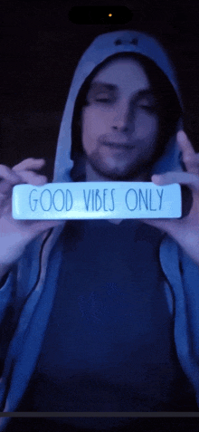 a man in a blue hoodie holds a sign that says good vibes only