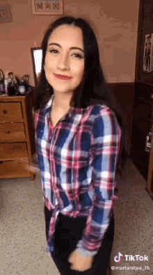 a woman wearing a plaid shirt and black pants is dancing in a room .