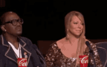 a man and a woman are sitting in front of a microphone with coca cola cups in front of them