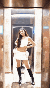 a woman in a white dress and black boots poses in an elevator