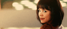 a close up of a woman 's face with short hair and bangs looking over her shoulder .