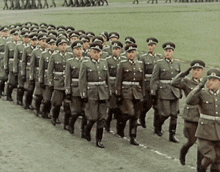 a large group of soldiers marching in a line with one wearing a hat with the letter t on it
