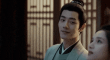 a man in a kimono is standing next to a woman in a room and smiling .