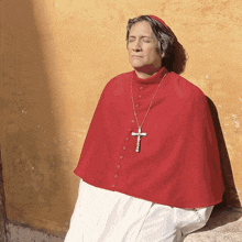 a man wearing a red cape and a cross necklace sits with his eyes closed