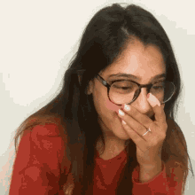 a woman wearing glasses and a red shirt is covering her mouth