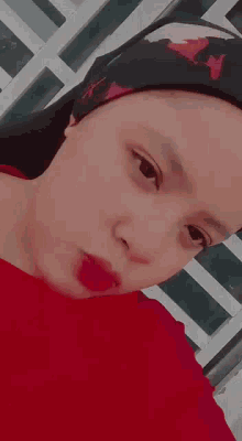 a woman wearing a red shirt and a black head scarf is looking at the camera