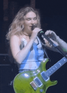 a blonde woman singing into a microphone while holding a green guitar