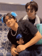a couple of young men sitting next to each other with one wearing sunglasses and a flower in his hair
