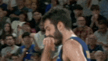 a basketball player with a beard is covering his mouth with his hand while standing in front of a crowd .