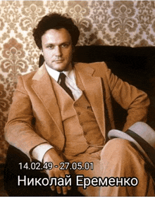 a man in a suit and tie sits in a chair with the date 14.02.49-27.05.01
