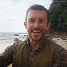 a man wearing glasses and a plaid shirt is smiling on a beach ..