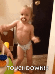a baby in diapers is dancing in a room with a pacifier in his mouth .
