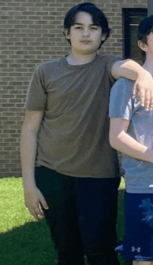 a young man in a brown shirt is standing next to another young man in a grey shirt .