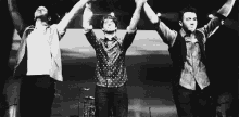 a black and white photo of three men holding hands in the air .
