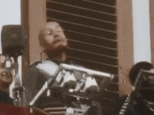 a man with a beard is standing in front of a microphone and talking into it .