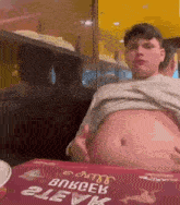 a man with a very large belly is sitting at a table with a box that says bokceb 21evk on it .
