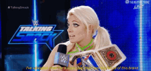 a woman is holding a wrestling championship belt and talking into a microphone on a wrestling show .