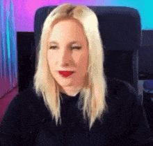 a blonde woman with red lipstick is sitting in a chair .