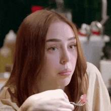 a woman with red hair is eating food with a fork and looking at the camera .