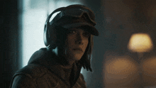 a woman wearing headphones and goggles has her finger to her mouth