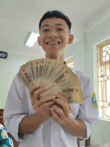 a young man is holding a fan of money with a sign in the background that says hiep