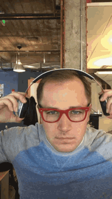 a man wearing red glasses holds a pair of headphones on his head
