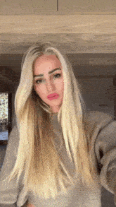 a woman with long blonde hair is wearing a grey sweater and making a funny face .