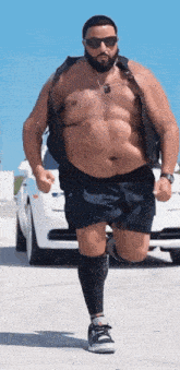 a shirtless man with a beard and sunglasses is running in front of a white car