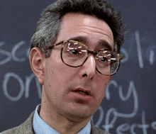 a man wearing glasses is standing in front of a blackboard with the word theory written in chalk