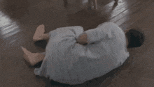 a man in a hospital gown is laying on the floor with his hands on his head .
