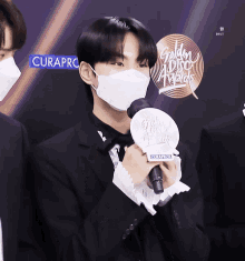 a man wearing a mask is holding a microphone in front of a sign that says golden music awards