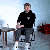 a man wearing a black hoodie with a bear on the front sits in a chair