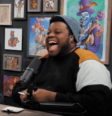 a man wearing a hat is laughing in front of a microphone in front of a wall of pictures