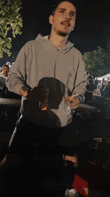a man wearing a grey sweatshirt that says ' a ' on it holds a glass