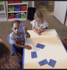a group of children are sitting at a table with blue cards with the letters h and j on them