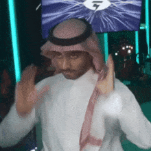 a man wearing a head scarf and a white shirt is dancing in front of a large screen with the number 7 on it