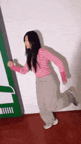 a woman in a pink and white striped shirt and gray pants is running in a room .