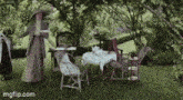 a woman in a hat is standing next to a table and chairs in a garden .