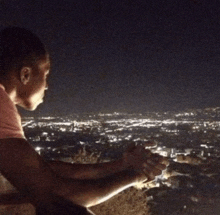 a man in a pink shirt is looking out over a city at night
