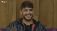 a man with a beard is smiling while sitting on a purple couch .