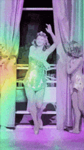a woman is dancing in front of a window with a rainbow background